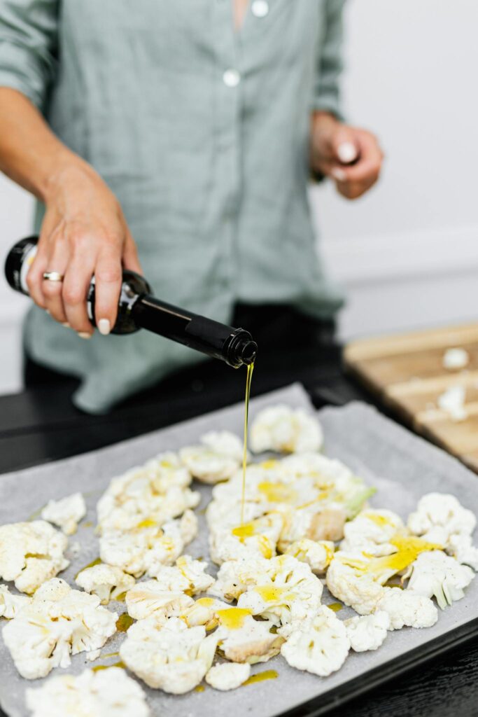 Close-up of a woman preparing a healthy keto meal by pouring olive oil on cauliflower florets.