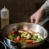 Close-up of sautéing broccoli and bell peppers in a pan on a stove.