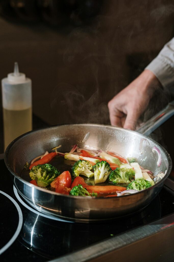 Close-up of sautéing broccoli and bell peppers in a pan on a stove.
